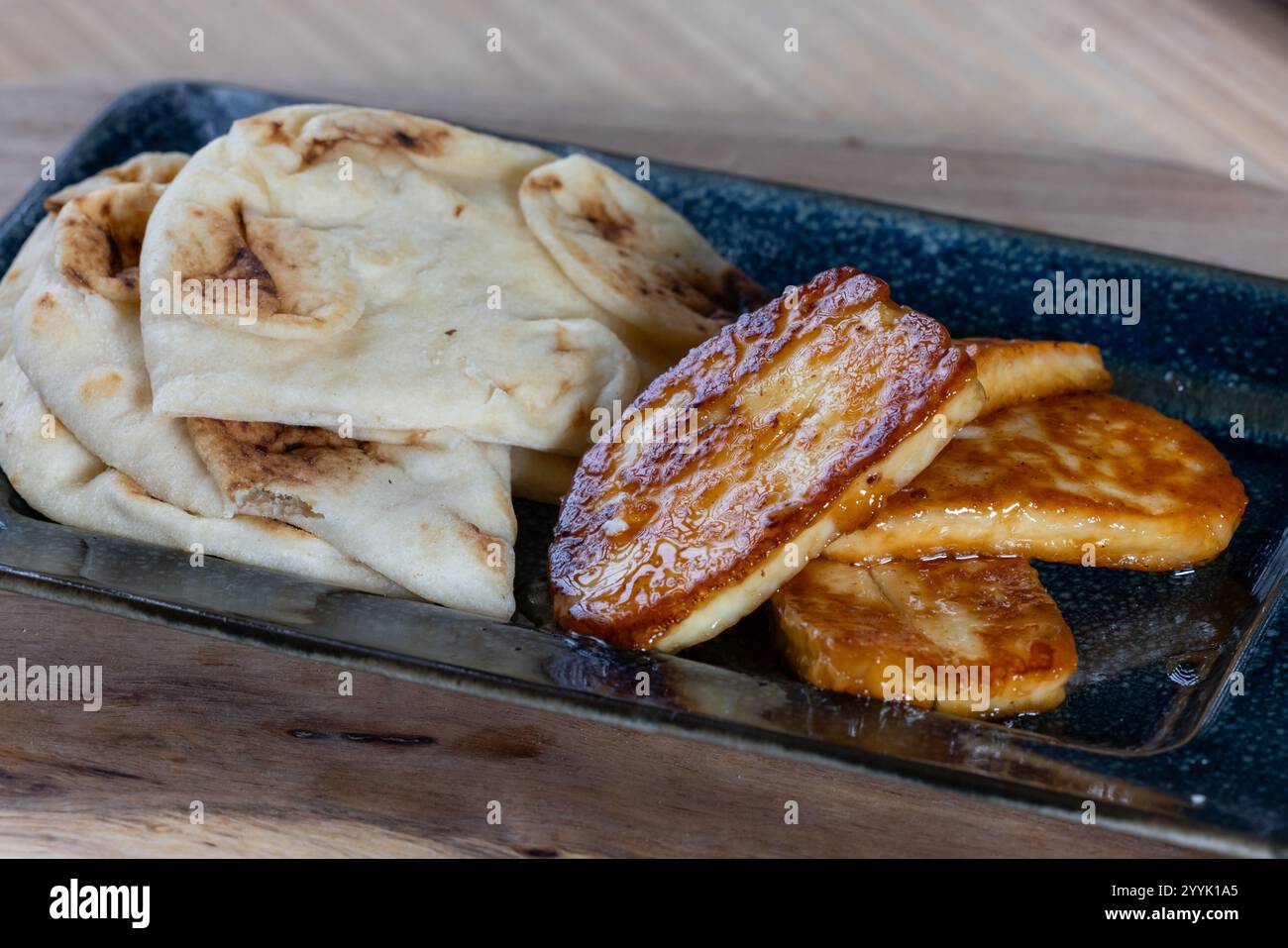 Ein Teller mit gebratenem halloumi-Käse mit einer Seite Pita-Brot. Das Essen ist goldbraun und sieht köstlich aus. Stockfoto
