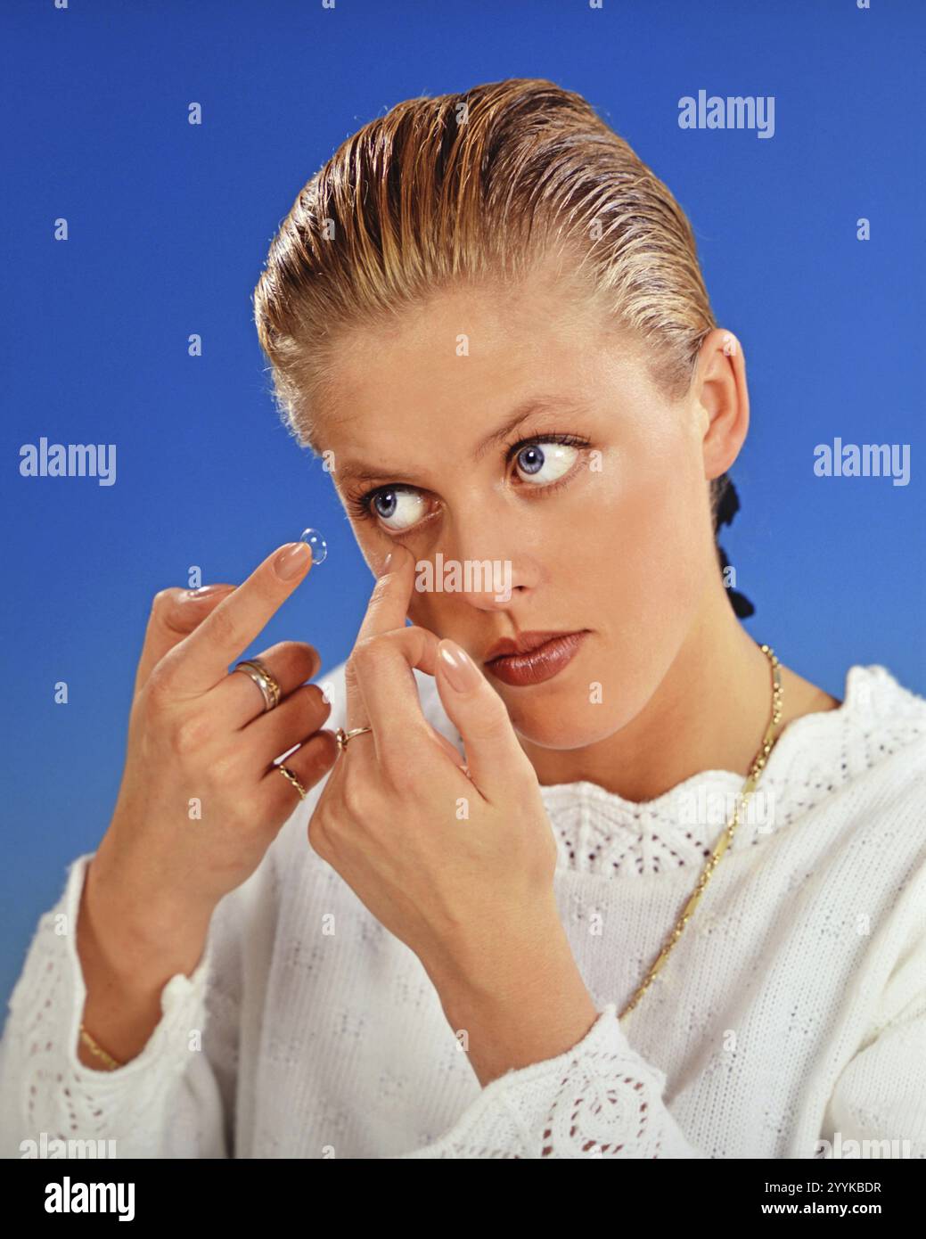 Eine blonde Frau führt eine Kontaktlinse ins Auge ein, 25 Jahre alt, Sehstörungen, Kontaktlinsen-Studiofoto, Niedersachsen, Bundesrepublik Keim Stockfoto