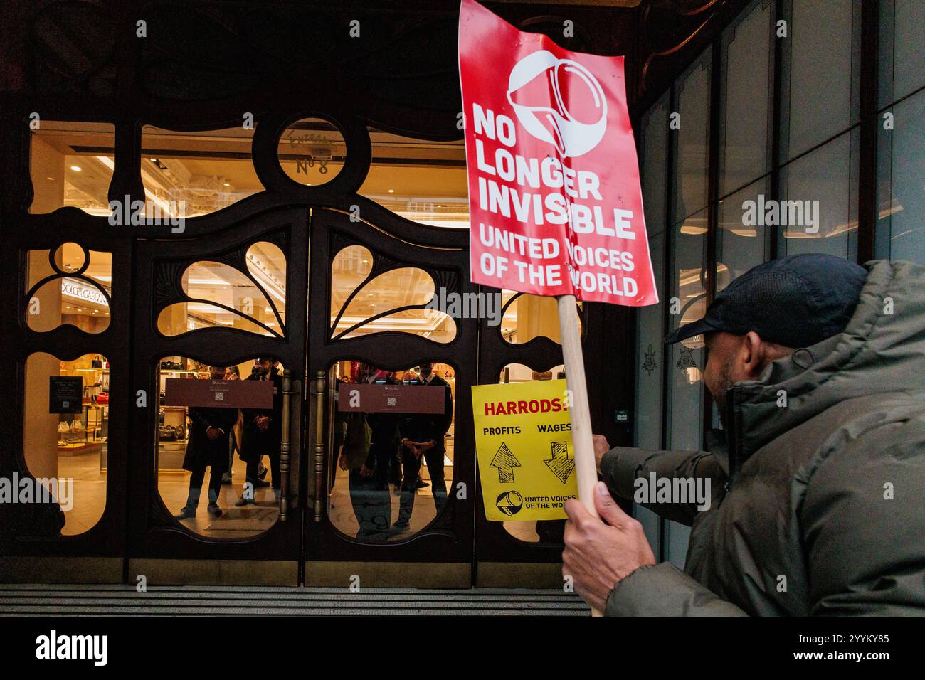 London, Großbritannien. Dezember 2024. Ein streikender Arbeiter, vertreten durch die gewerkschaft United Voices of the World (UVW), steht mit Schildern vor dem Kaufhaus Harrods. UVW-Mitglieder, die überwiegend Wanderarbeiter sind, ergreifen Arbeitskampfmaßnahmen gegen eine neue „Harrods Leave Policy“, die ihre Möglichkeiten, sich für einen Besuch ihrer Familien im Ausland freizumachen, stark einschränkt. Markante UVW-Sicherheitsleute aus dem Science Museum, dem Natural History Museum und dem Victoria & Albert Museum waren ebenfalls an der Streiklinie vor Harrods anwesend. Quelle: Mark Ke Stockfoto