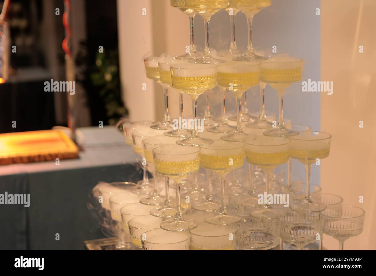 Hoch aufragende Pyramide aus Sektgläsern gefüllt mit Sekt, elegant angeordnet vor einem rosafarbenen Hintergrund, perfekt für gehobene Feiern und Hochzeiten Stockfoto