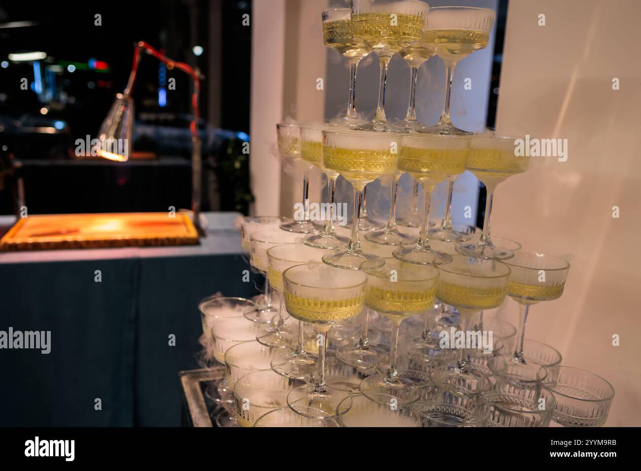 Hoch aufragende Pyramide aus Sektgläsern gefüllt mit Sekt, elegant angeordnet vor einem rosafarbenen Hintergrund, perfekt für gehobene Feiern und Hochzeiten Stockfoto