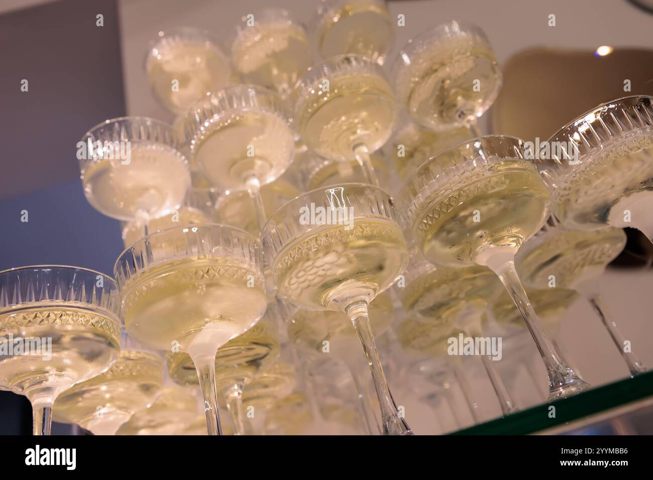Hoch aufragende Pyramide aus Sektgläsern gefüllt mit Sekt, elegant angeordnet vor einem rosafarbenen Hintergrund, perfekt für gehobene Feiern und Hochzeiten Stockfoto