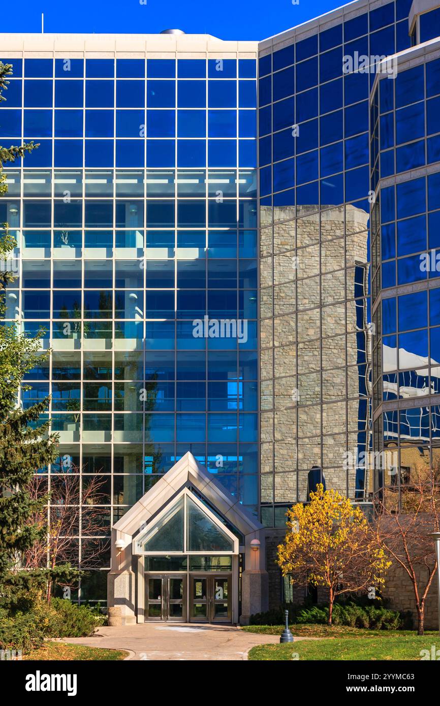 Ein großes Gebäude mit einer Glasfassade und einem großen Bogengang. Das Gebäude ist von Bäumen umgeben und hat viele Glasfenster Stockfoto