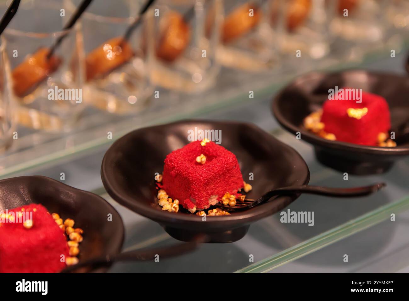 Köstliche rote Mini-Samtkuchen mit Frischkäse-Zuckerguss und geriebenem Käse, auf einem Regal angeordnet, serviert am Büfett Stockfoto