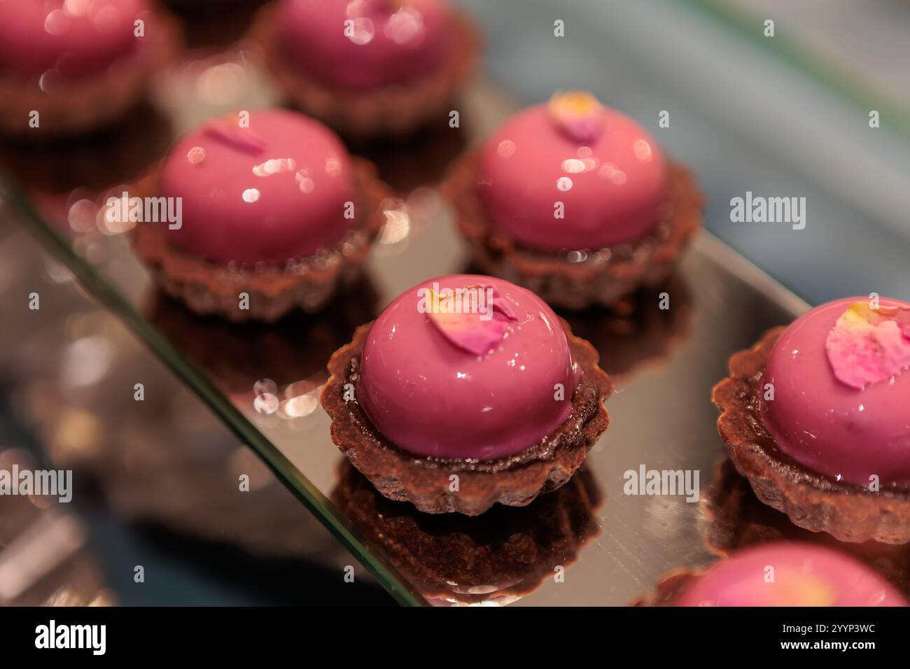 Eleganter Mousse-Kuchen mit cremiger Füllung und einer überraschenden Erdbeermarmelade, mit einer glatten rosafarbenen Glasur überzogen und mit gefriergetrockneter Raspel bestreut Stockfoto