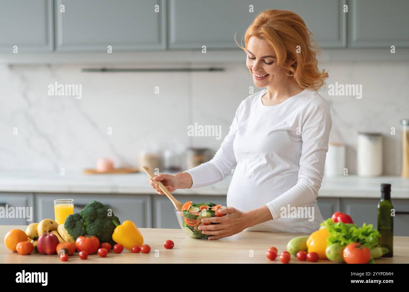 Schwangere Frau, die einen frischen Salat in einer modernen Küche zuhause zubereitet Stockfoto