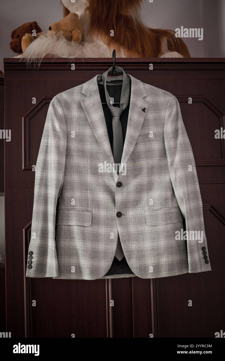Elegante graue, karierte Anzugsjacke, die an einer Holzgarderobe hängt. Stockfoto