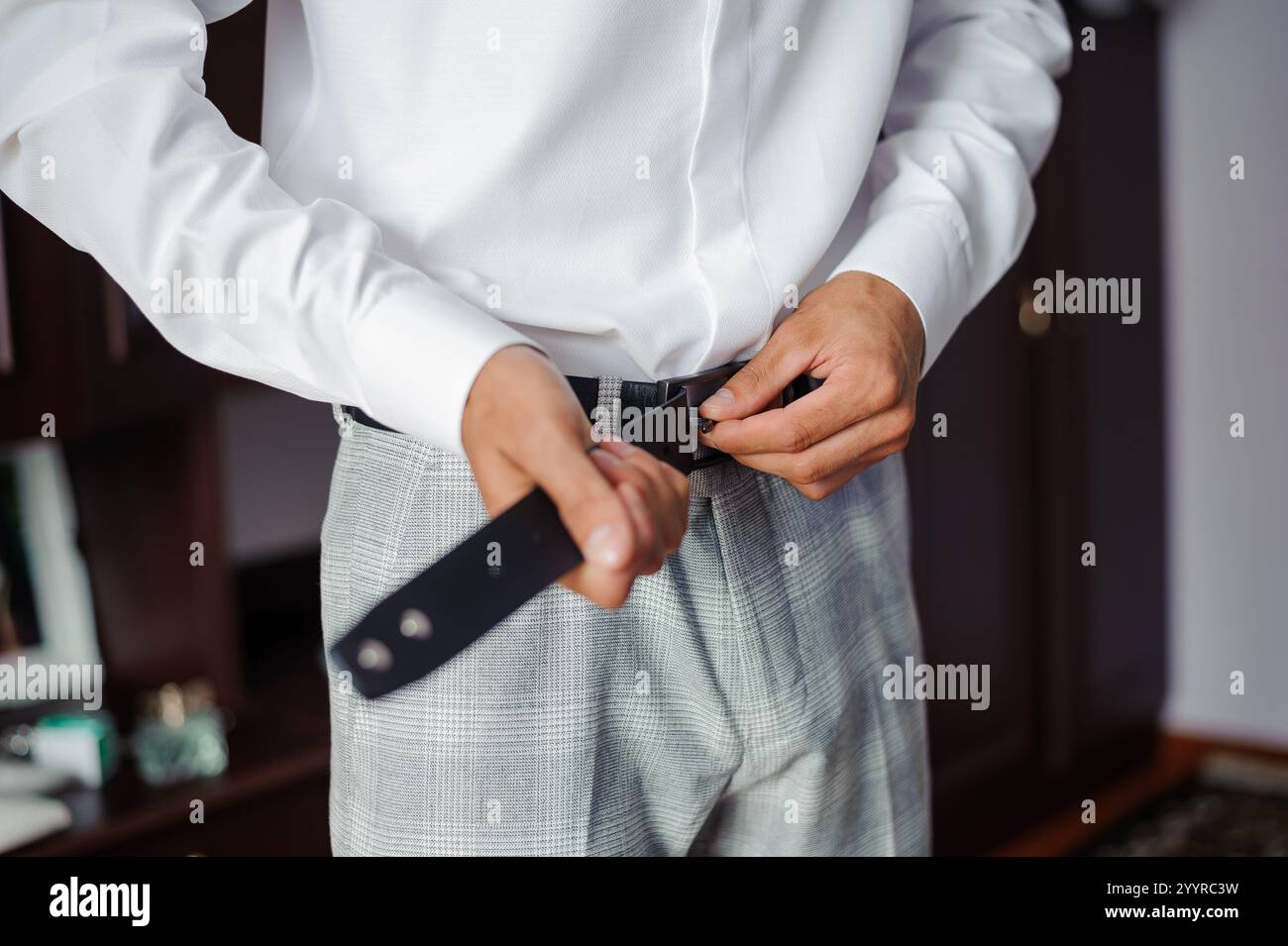 Eleganter Mann, der seinen Gürtel anpasst, bevor er sich für eine formelle Veranstaltung anzieht. Stockfoto