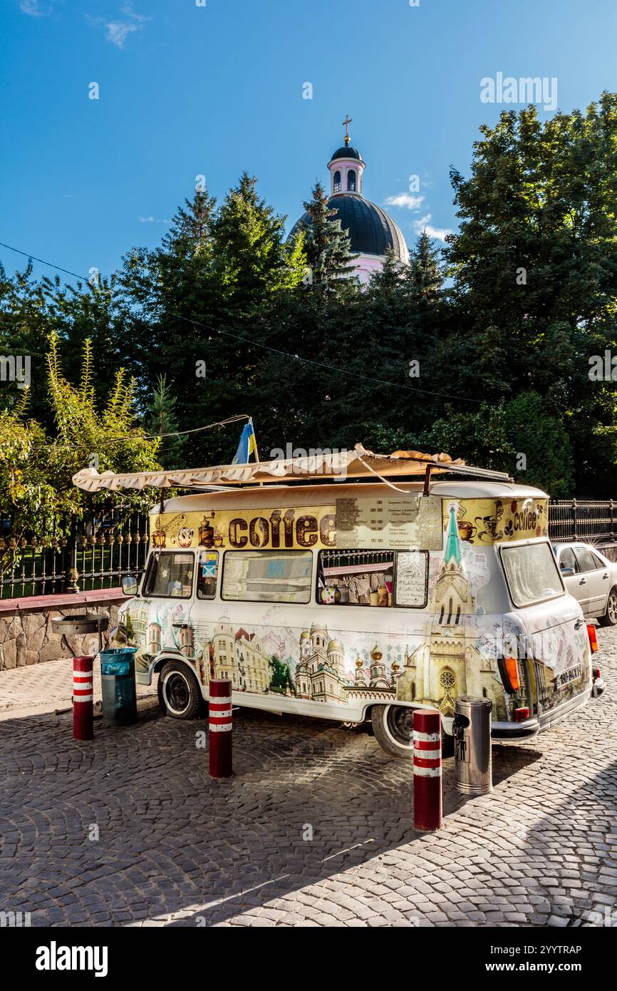 Ein weißer Food Truck mit farbenfrohem Design und dem Wort „Kaffee“ auf der Seite. Der Lkw steht vor einem Gebäude mit Uhrturm Stockfoto