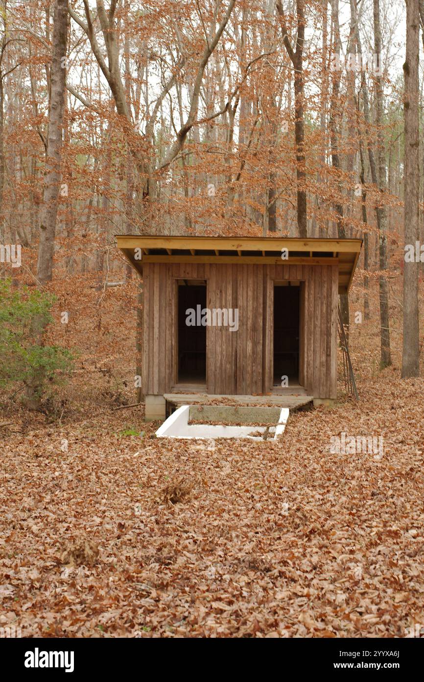 Alt draußen im Wald, eine im Boden liegende Quelle, die Weiße Taufe gespeist hat. Kleines Gebäude mit zwei Türen dahinter. Isolierter, eingebetteter Schatten mit Bäumen und braunem d Stockfoto