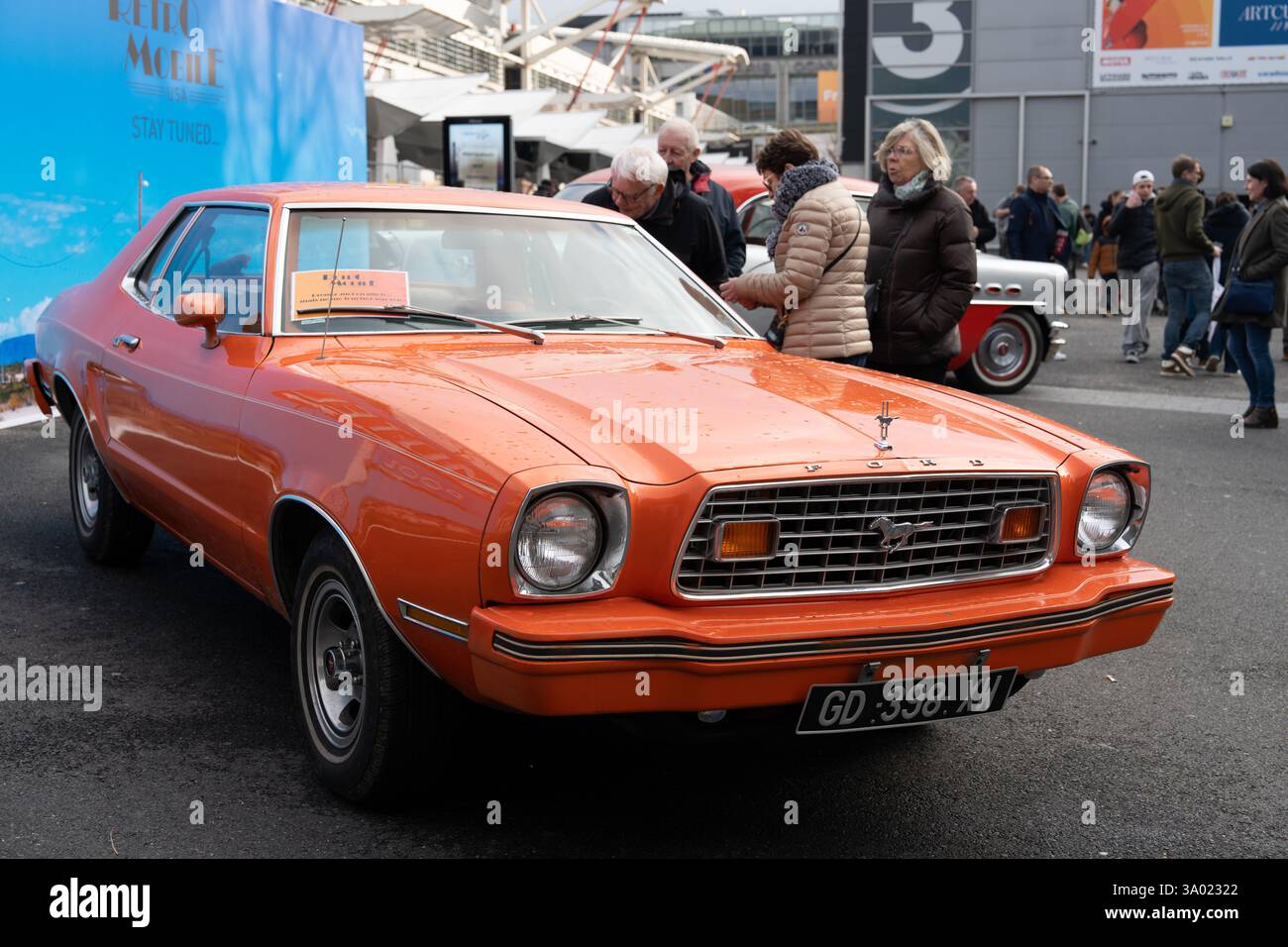 Ein Oldtimer in Orange zeigt Retro-Stil bei einem Treffen von Autoenthusiasten auf dem belebten Stadtplatz an einem sonnigen Nachmittag Stockfoto