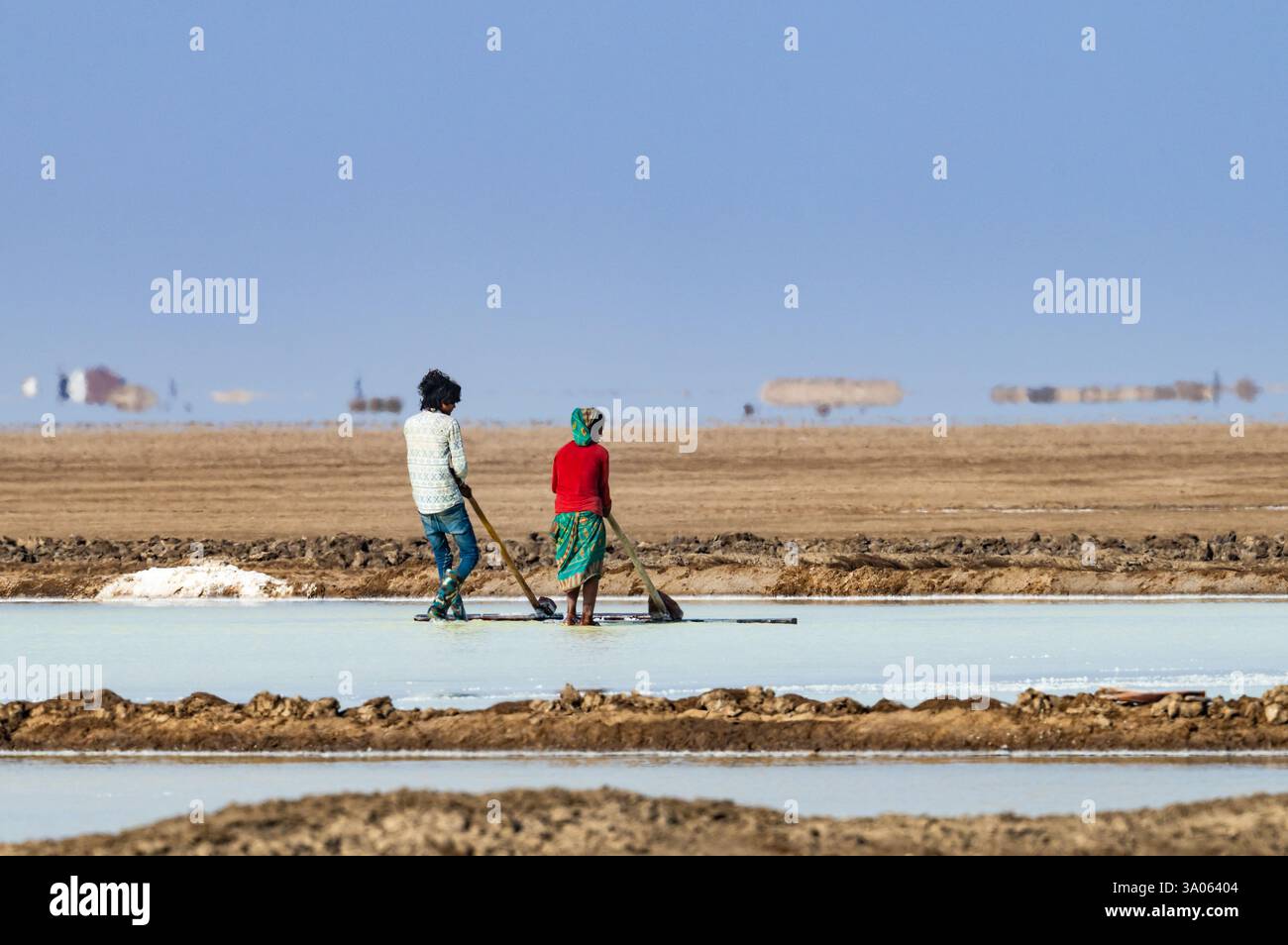 Ein indisches Paar, das Salz in einem Verdunstungsteich reckt. Gujarat, Indien. Stockfoto