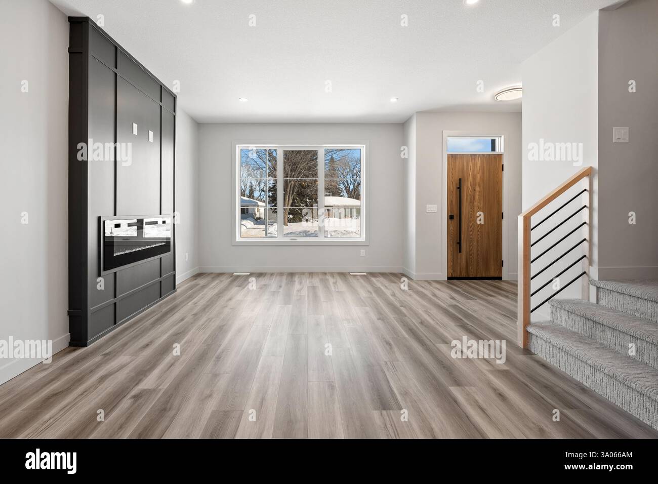 Großes, leeres Wohnzimmer mit Kamin und Treppe. Das Zimmer ist sehr sauber und gut beleuchtet, was ihm eine einladende und gemütliche Atmosphäre verleiht Stockfoto