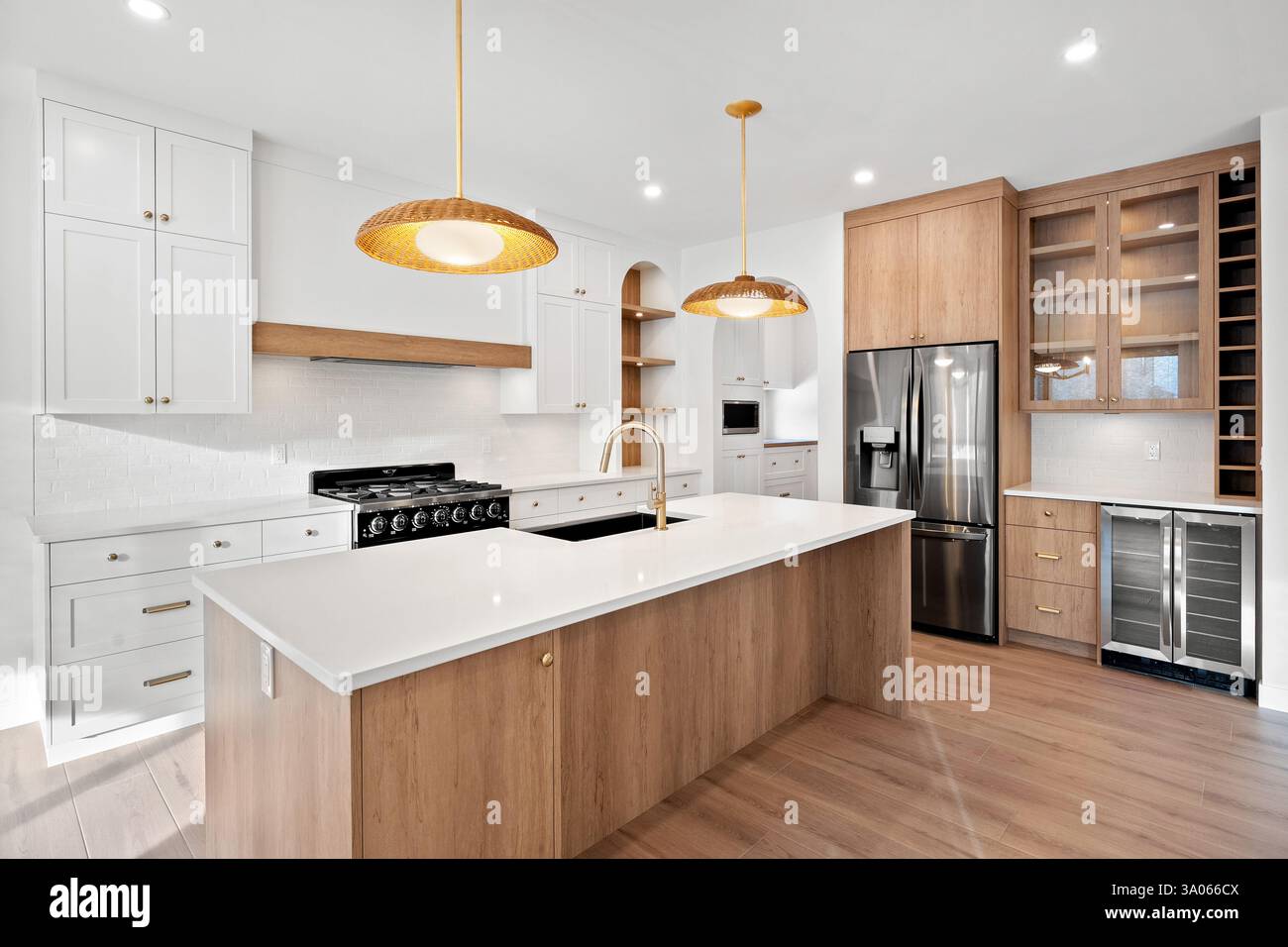 Küche mit einer weißen Insel und einem Edelstahl-Kühlschrank. Die Küche ist gut beleuchtet und hat eine warme, einladende Atmosphäre Stockfoto