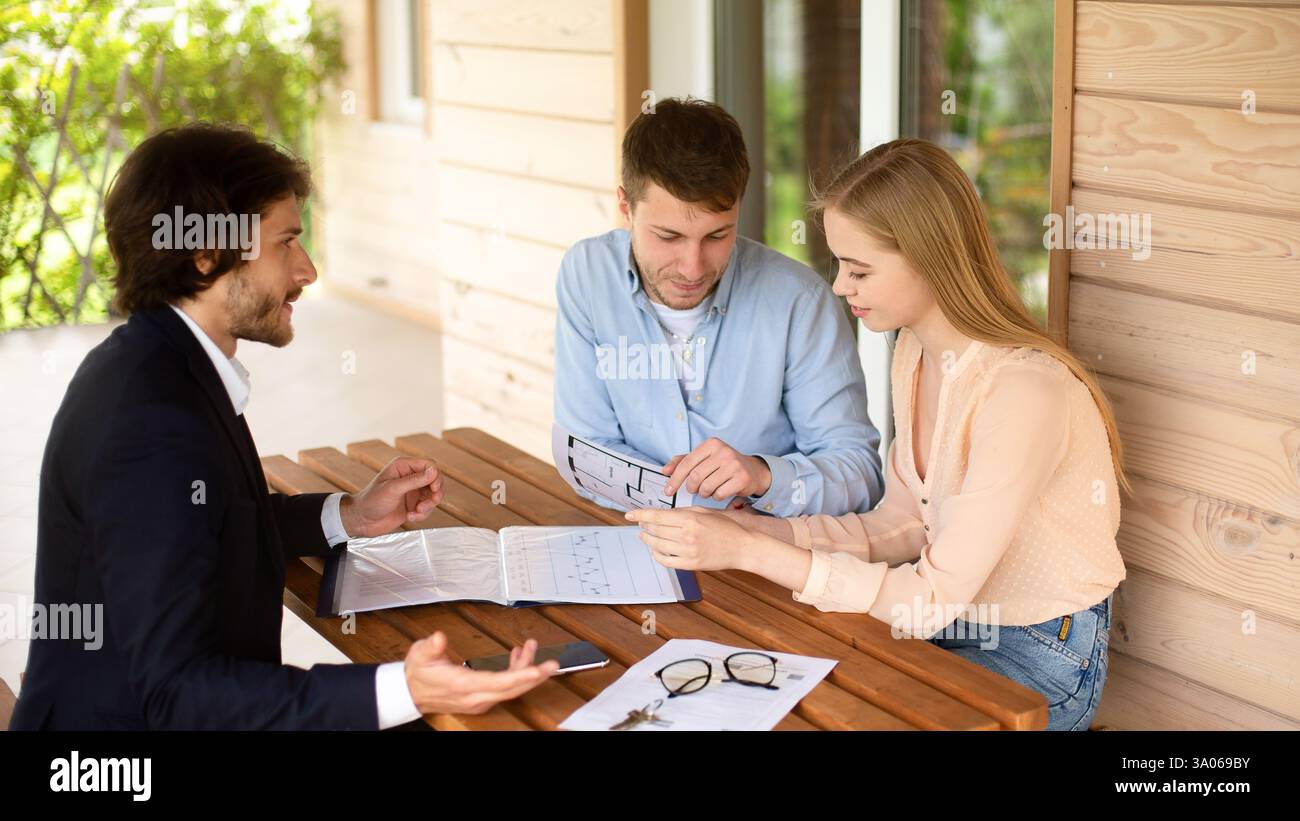 Immobilienmakler zeigt Hausprojekt für junge Familie auf der Veranda Stockfoto