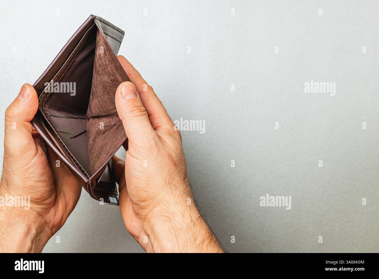 Ein Mann hält eine leere Ledertasche und symbolisiert finanzielle Not und den Stress der Budgetierung. Seine Finger zeigen das Fehlen von Geld und Ersparnissen, h Stockfoto