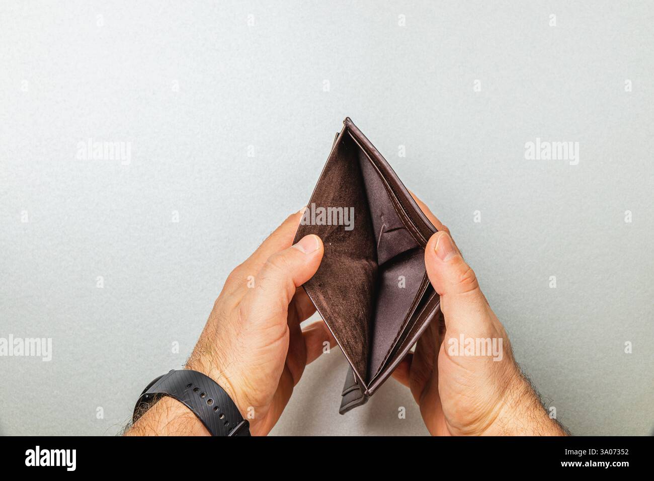 Ein Mann untersucht seine leere Geldbörse und symbolisiert die harte Realität der finanziellen Not. Er stellt sich den Herausforderungen der Budgetierung, der Ausgaben und des Verlusts Stockfoto