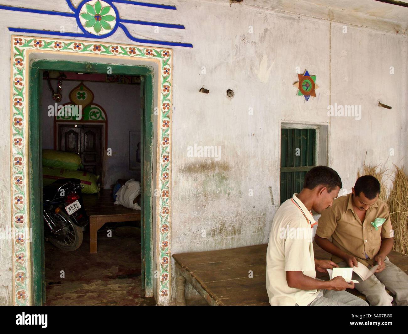 Dekorierte Tür eines Hauses in Bakraur, dem Land Sujata, in der Nähe von Bodh Gaya, Bihar, mit zwei Männern, die draußen mit Papierkram beschäftigt waren. Stockfoto