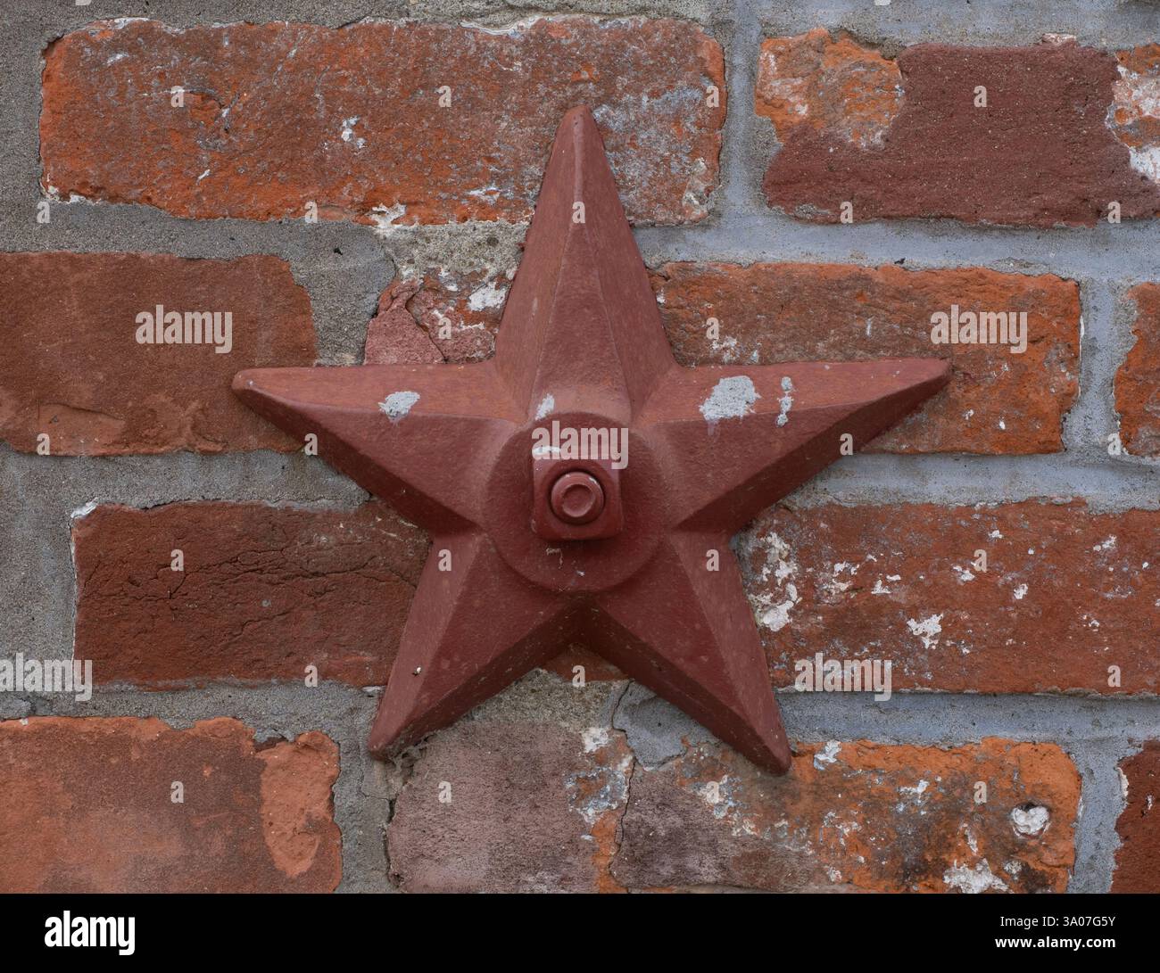 Nahaufnahme eines rotbraun lackierten Metallsterns, der an eine alte Ziegelmauer verschraubt ist. Stockfoto