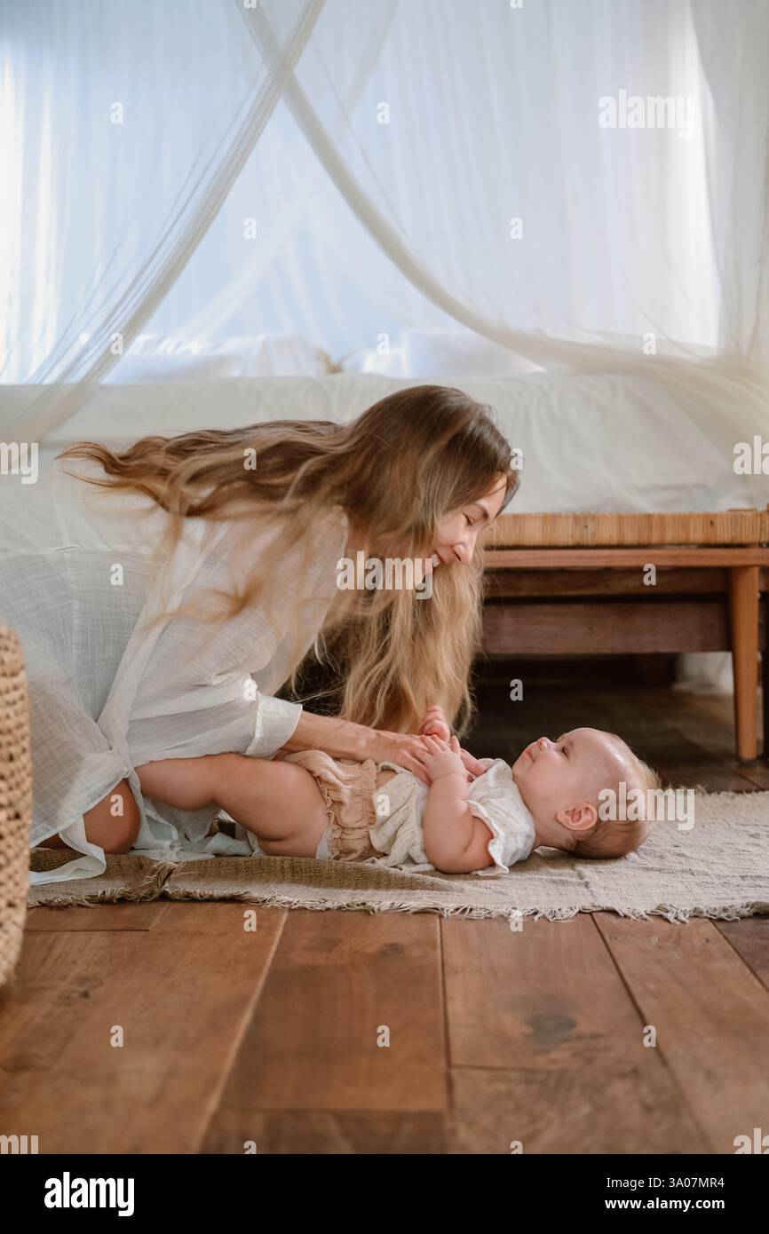 Ein Baby liegt auf der Decke und lacht, Mama spielt mit ihr. Kitzelt Tochter. Stockfoto