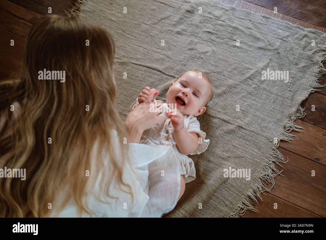 Ein Baby liegt auf der Decke und lacht, Mama spielt mit ihr. Kitzelt Tochter. Stockfoto