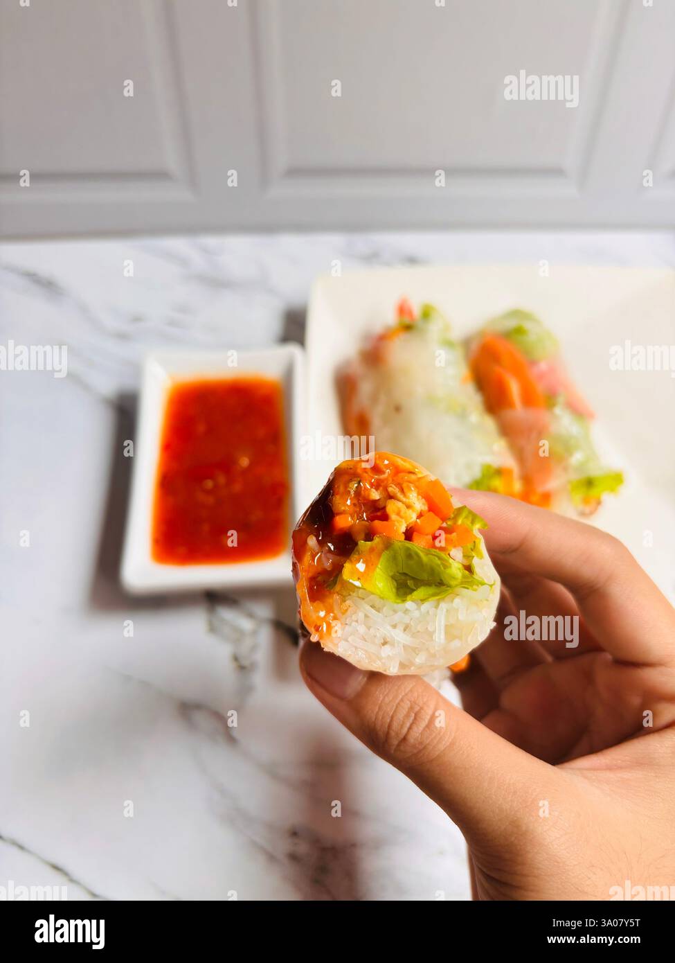 Eine Nahaufnahme einer köstlichen Reispapierrolle mit frischem Salat, knusprigen Karotten, Vermicelli-Nudeln und aromatischem Protein - Smartphone-aufgenommenes Stockfoto