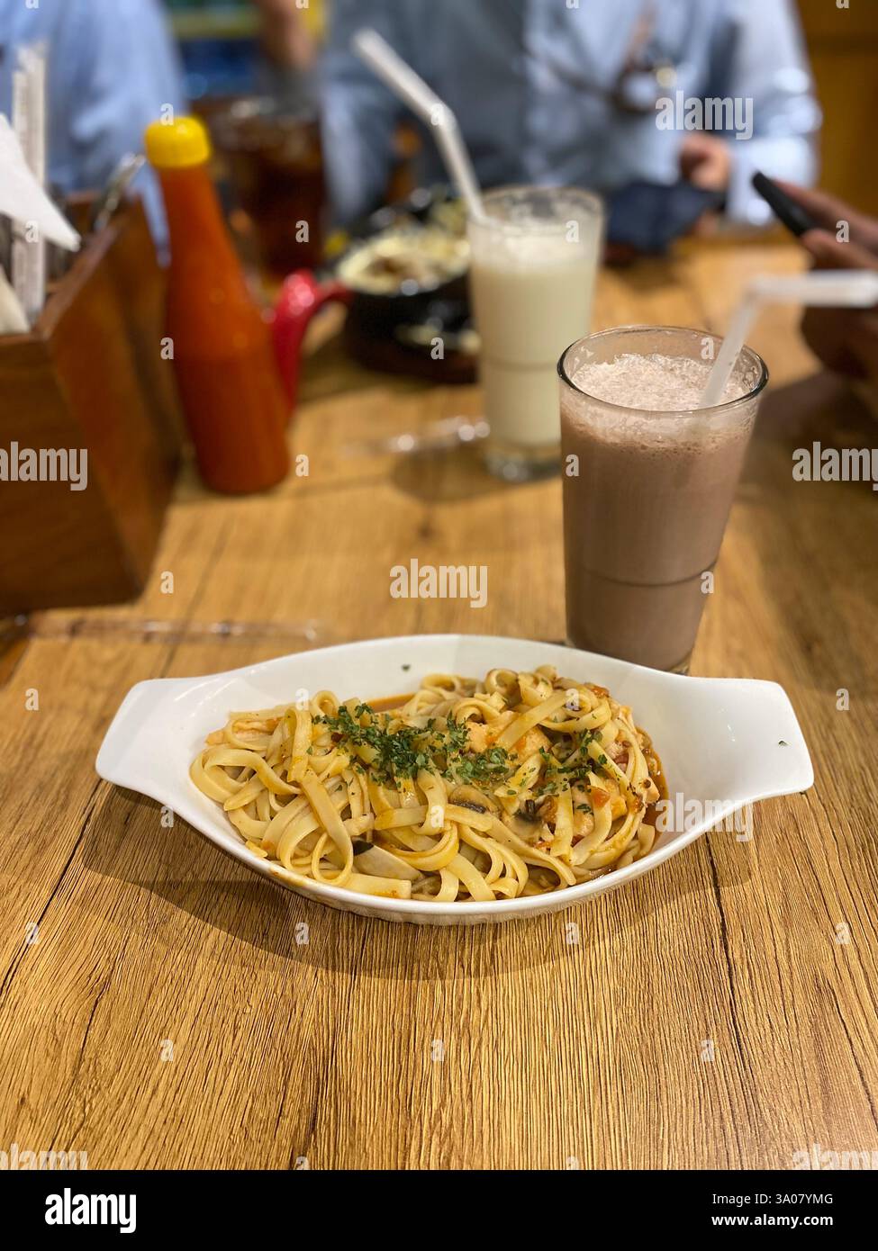 Ein köstlicher Pasta-Teller, serviert mit einem reichhaltigen Schokoladenshake, in gemütlichem Restaurant-Ambiente. Perfekt für Feinschmecker und Restaurantfans. Stockfoto