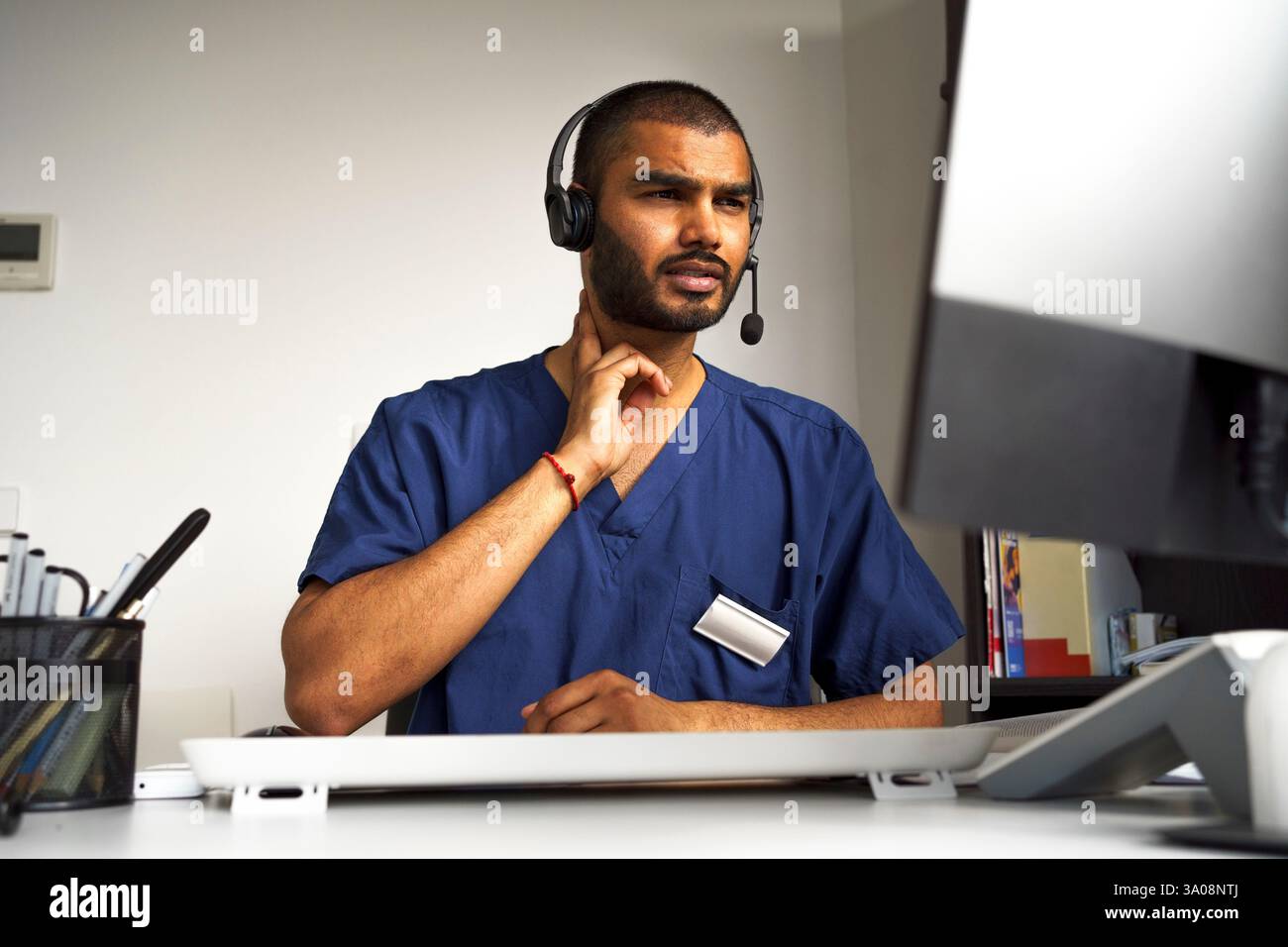 Tiefwinkelansicht eines männlichen Arztes, der den Hals berührt und mit dem Patienten im Videogespräch in der Klinik kommuniziert Stockfoto