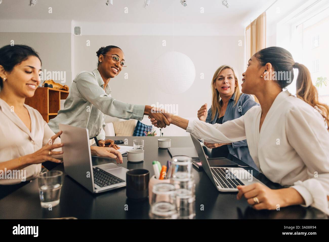 Glückliche junge Unternehmerin schüttelt sich bei einem Treffen im Kreativbüro die Hand mit einer Kollegin Stockfoto