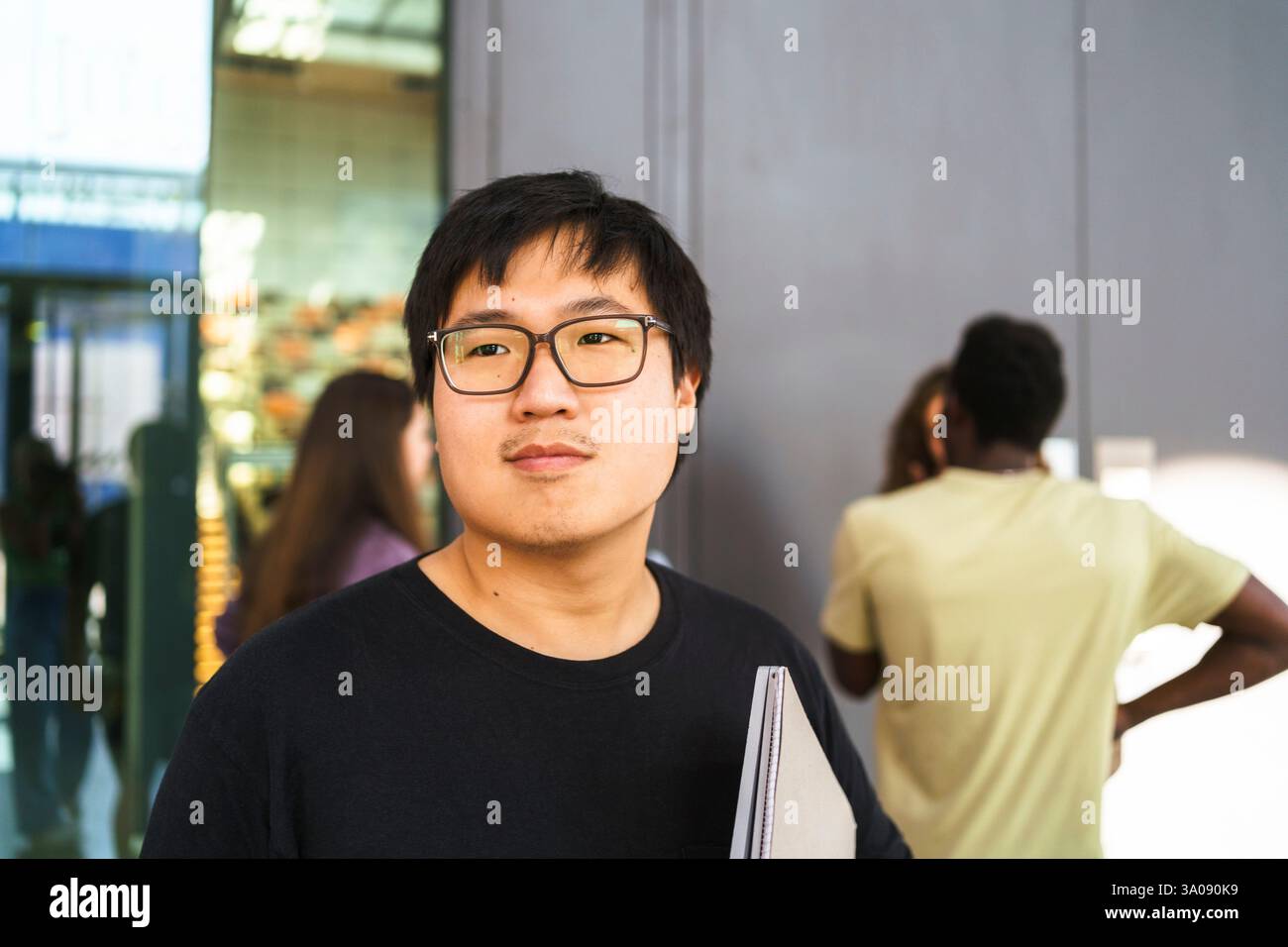 Junger männlicher Student mit Brille, der auf dem College-Campus wegschaut Stockfoto