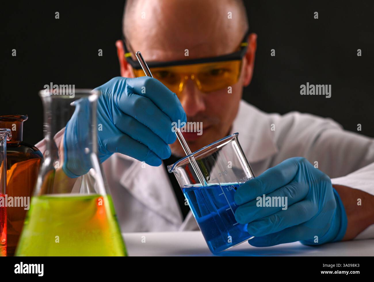 Wissenschaftler mit Schutzbrille und Handschuhen mischen während des Forschungsversuchs sorgfältig blaue chemische Lösung im Laborbecher. Stockfoto