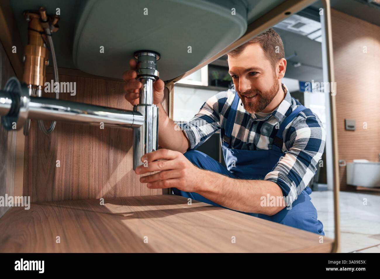 Nahansicht. Wasserhahn wird befestigt. Klempner in blauer Uniform arbeitet im Badezimmer. Stockfoto