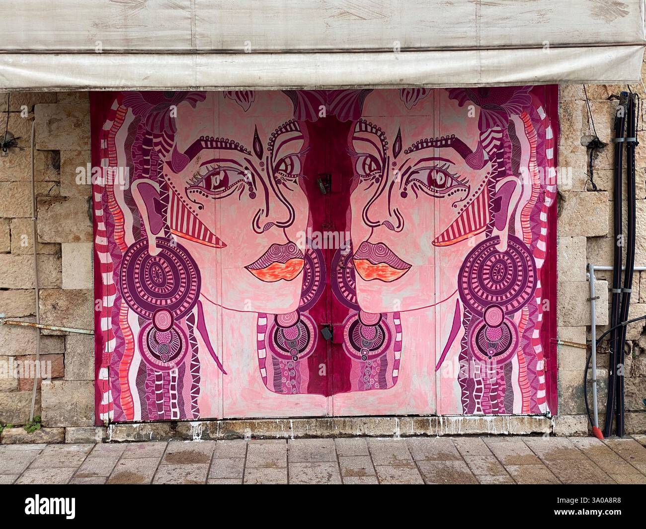 Lebendige Straßenkunst in Tel Aviv, Israel, die zwei abstrakte, von Stämmen inspirierte weibliche Figuren auf einer rustikalen Steinmauer zeigt. Dieses auffällige und ausdrucksstarke Wandgemälde Stockfoto