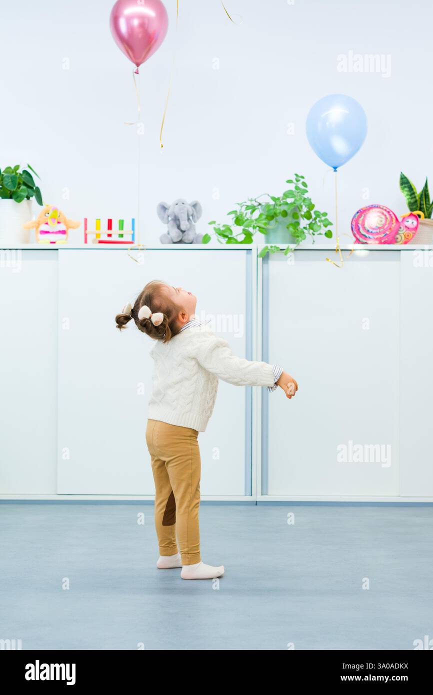 Niedliches 3-jähriges Mädchen mit Down-Syndrom feiert ihren Geburtstag in einem mit Ballons dekorierten Spielzimmer. Kindergeburtstag. Stockfoto