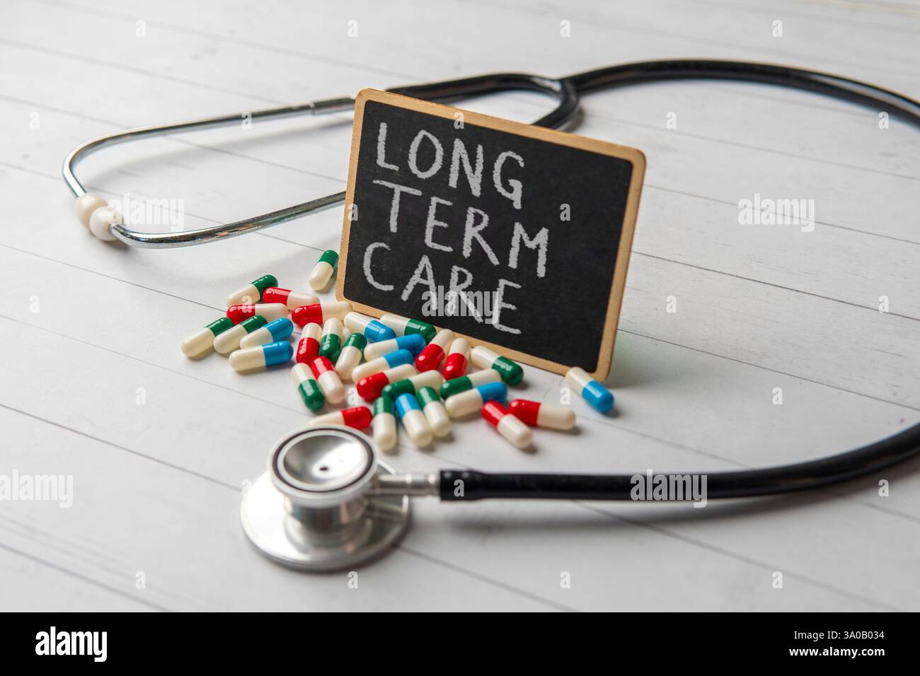 Eine Tafel mit den Worten "LANGZEITPFLEGE", umgeben von verstreuten Pillen und einem Stethoskop. Medizin- und Gesundheitskonzept. Stockfoto
