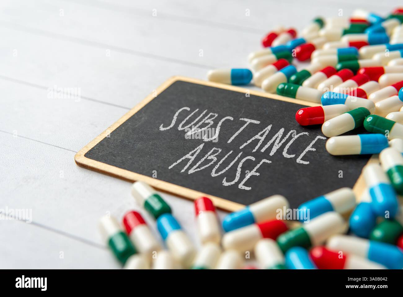 Eine Tafel mit den Worten "SUBSTANZMISSBRAUCH" umgeben von verstreuten Pillen und Kapseln. Medizin- und Gesundheitskonzept. Stockfoto