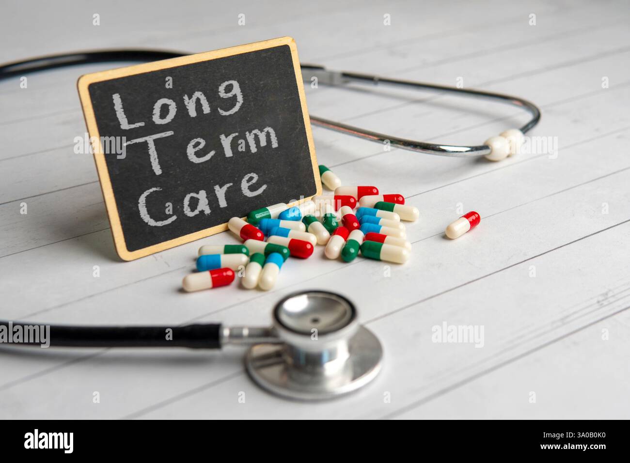Eine Tafel mit den Worten "LANGZEITPFLEGE", umgeben von verstreuten Pillen und einem Stethoskop. Medizin- und Gesundheitskonzept. Stockfoto
