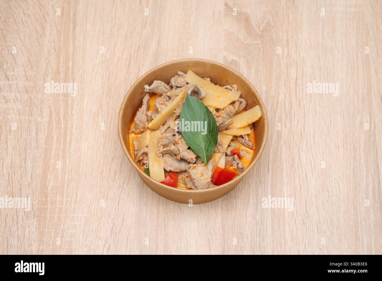 Thailändisches Rindfleisch in Pappbehälter zum Mitnehmen auf hölzernem Hintergrund. Internationale Küche Stockfoto