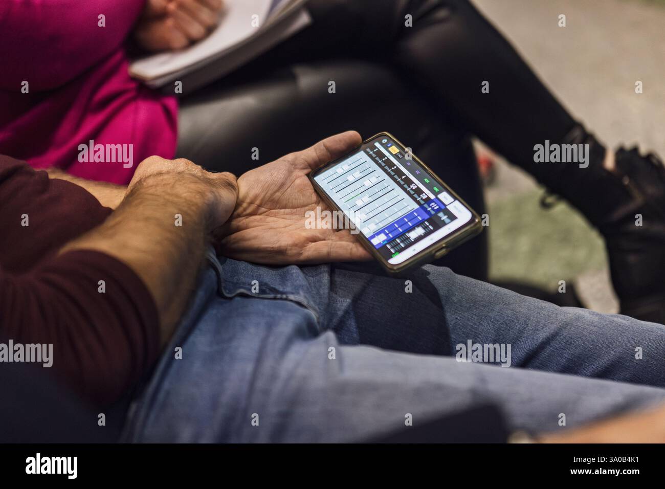 Nahaufnahme von Tontechnikern, die während der Besprechung im Aufnahmestudio ein Smartphone mit mobiler Audio-Mischanwendung halten Stockfoto
