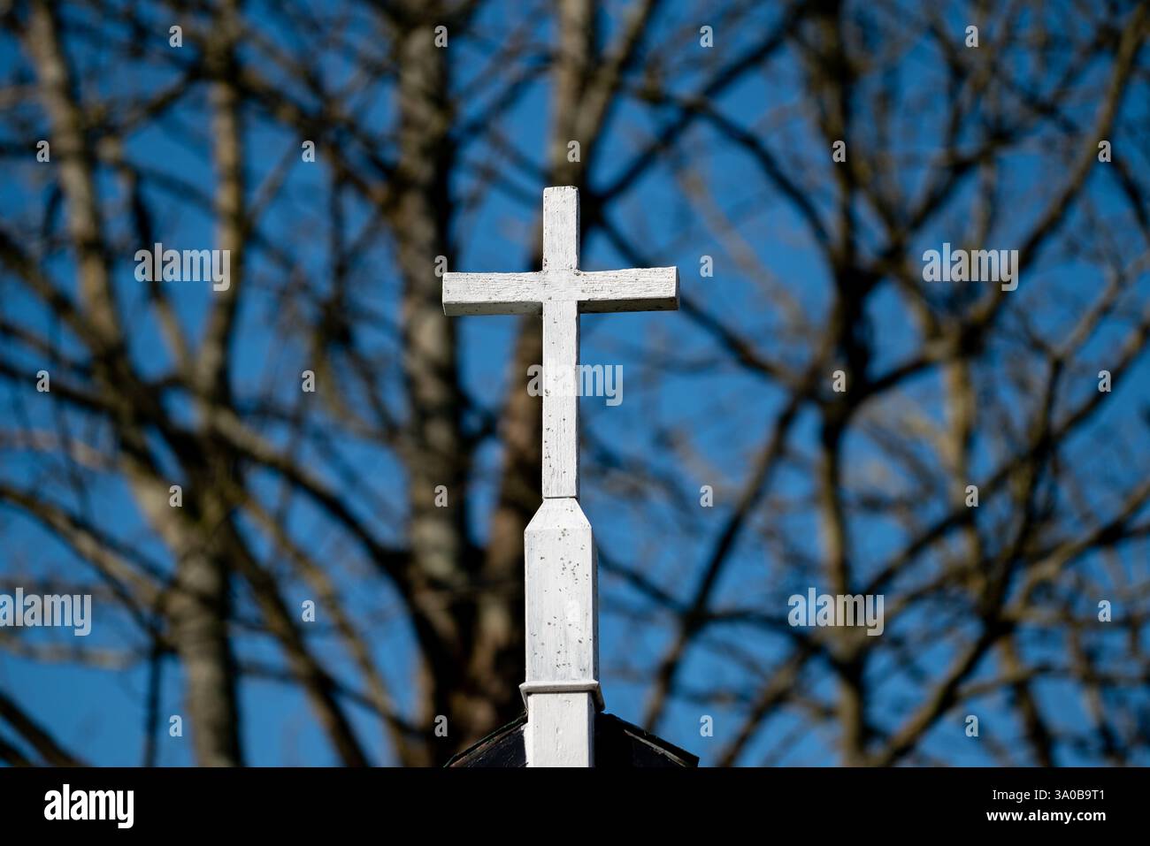 Hellweiß lackiertes Holzkreuz mit einem unscharfen Hintergrund von Bäumen. Stockfoto
