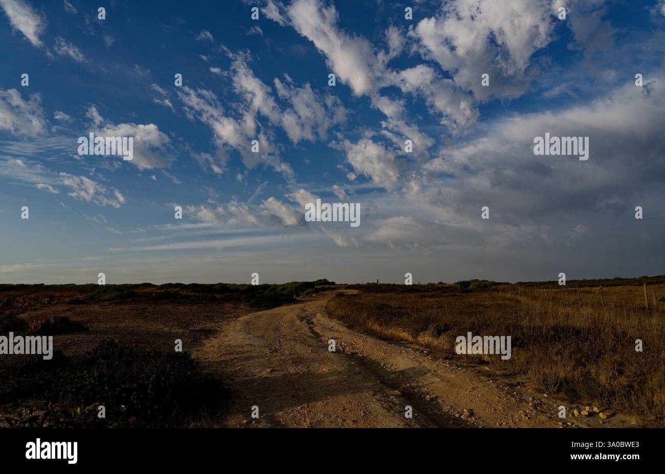 Die gewundene, unbefestigte Straße zieht sich durch die zerklüftete Landschaft von Baixo Alentejo, unter einem Himmel voller Wolken Stockfoto