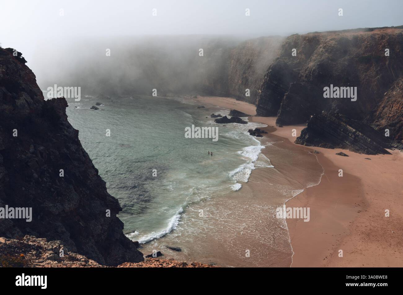 Goldener Sand und türkisfarbene Wellen treffen auf zerklüftete Klippen, während der Nebel über Praia do Tonel rollt Stockfoto