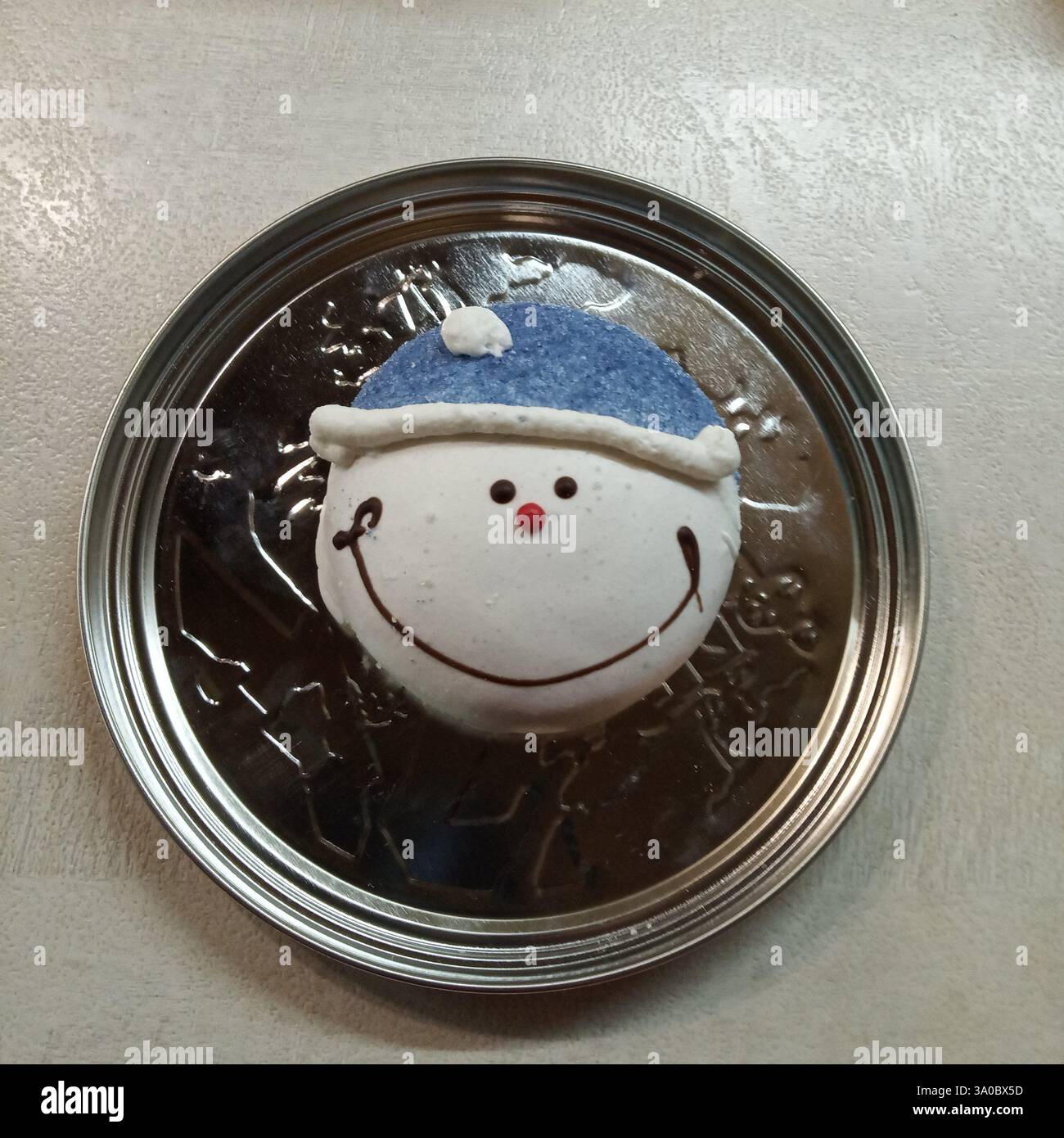 Ein lächelnder Schneemann-Lebkuchenkeks auf einer metallischen Oberfläche, der einen reizvollen Kontrast zwischen der Wärme der festlichen Leckerei und der Kuh schafft Stockfoto