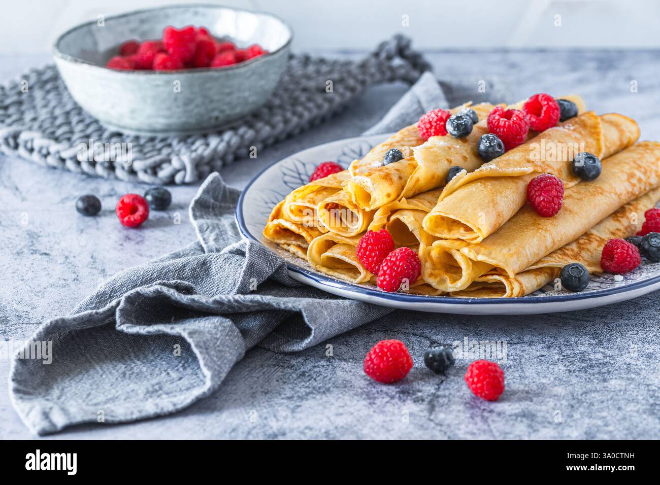 Teller mit gerollten Pfannkuchen mit Rasperries und Heidelbeeren auf hellblauem Hintergrund Stockfoto