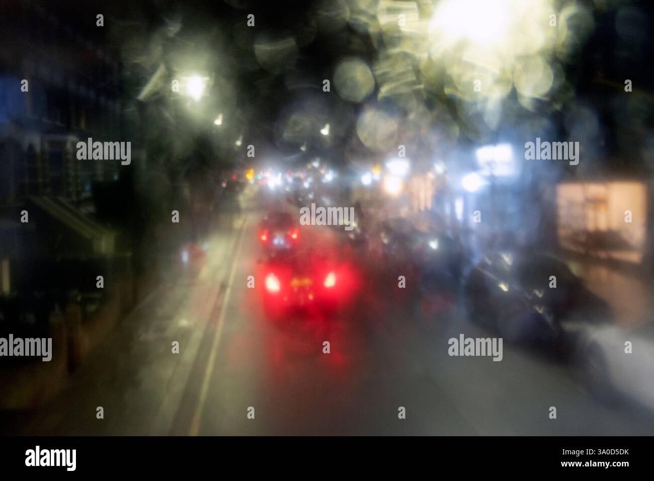 Verschwommene Sicht auf bunte rote Hecklichter im Straßenverkehr nachts durch einen Doppeldeckerbus im Obergeschoss, ein regnerisches Fenster in London, Großbritannien Stockfoto