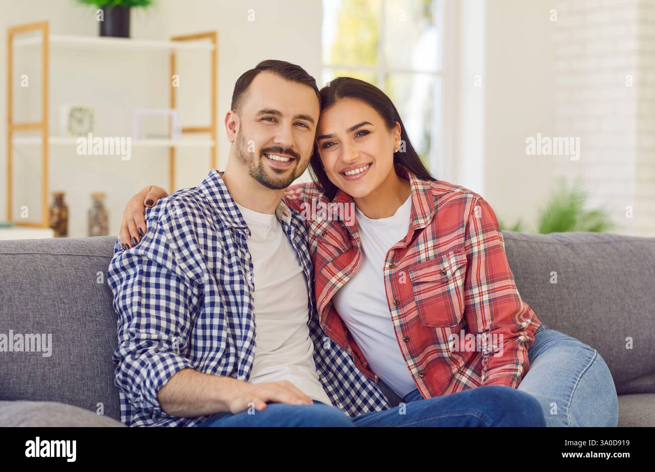 Junge glückliche verheiratete Paare sitzen auf dem Sofa im Wohnzimmer zu Hause und lächeln. Stockfoto