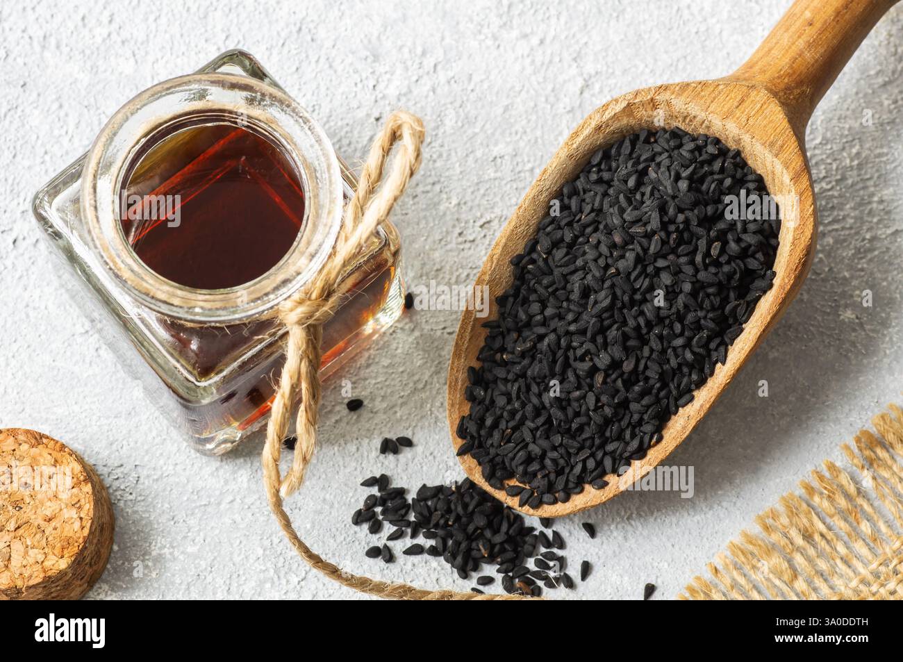 Glasflasche des ätherischen Öls der Schwarzkümmelsamen, Nigella Sativa im Löffel auf rustikalem Hintergrund. Organische Kräutermedizin für viele Krankheiten, Schwarzkümmel Stockfoto