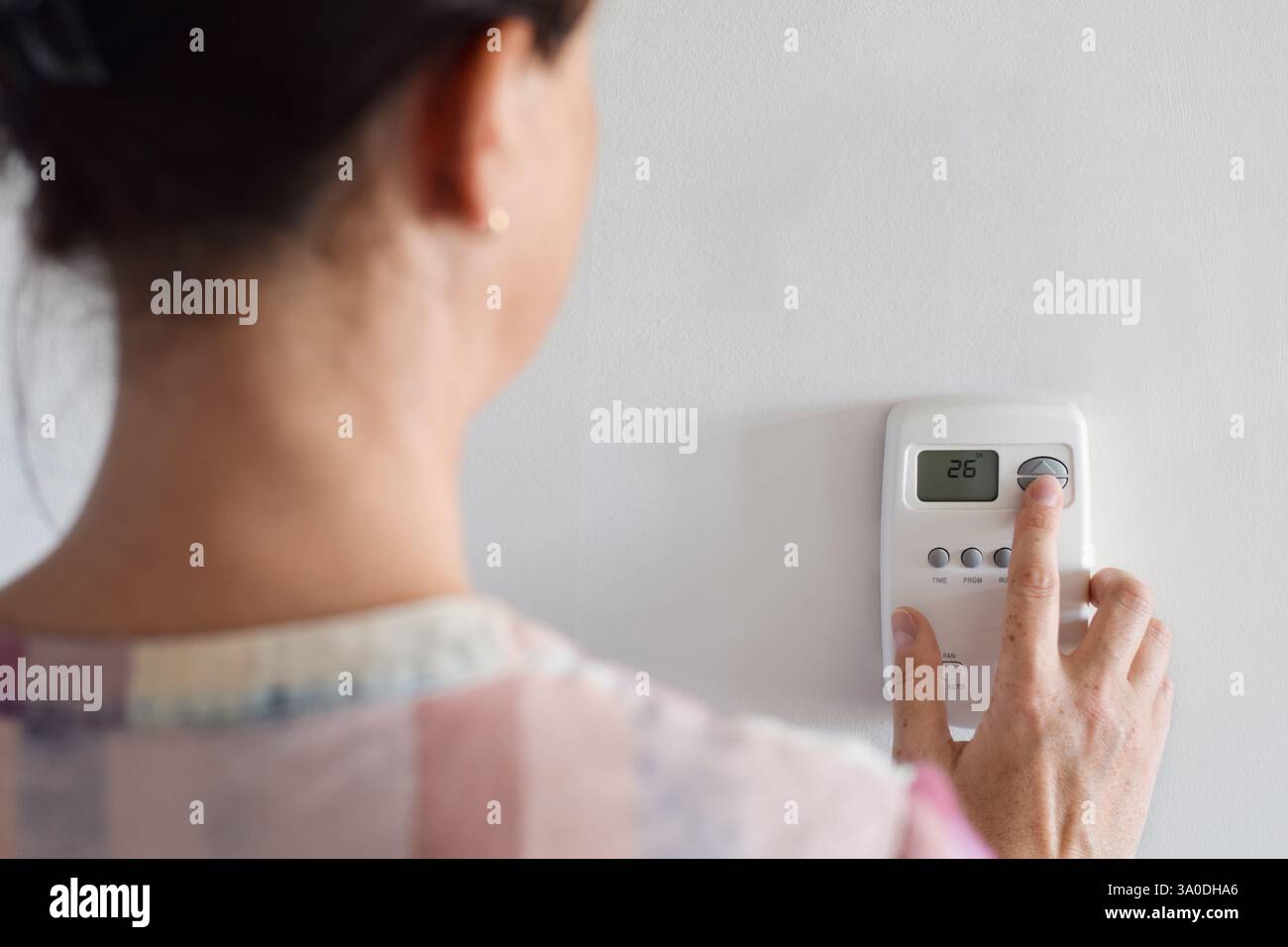 Frau von hinten, die die Temperatureinstellungen des Thermostats anpasst Stockfoto