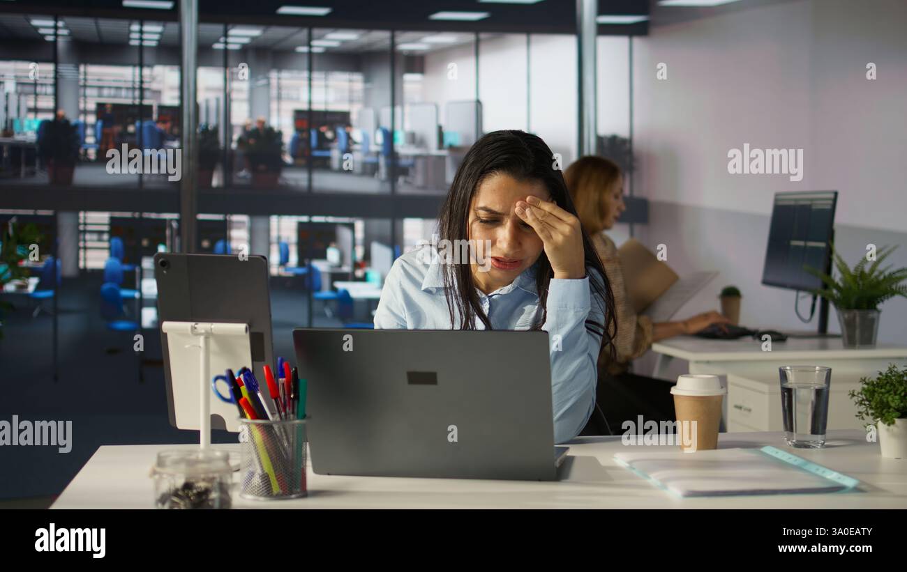 Eine gestresste Geschäftsfrau an ihrem Laptop fühlt den Druck von Projektterminen und emotionalen Belastungen. Unwell General Manager hat mit Migräne und Burnout zu kämpfen, was ihren Arbeitstag zu einer Herausforderung macht. Kamera B.. Stockfoto