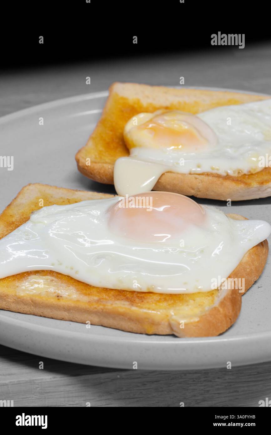 Spiegelei auf Toast auf einem grauen Steingut-Teller mit Holzbrett Hintergrund. Traditionelles Frühstücksessen. Stockfoto